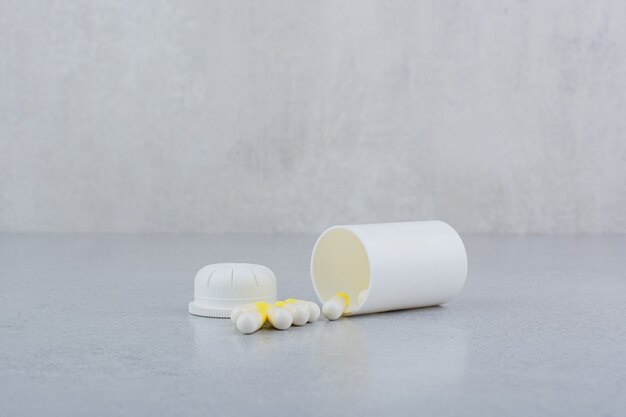 Kapsułki farmaceutyczne z plastikowego białego pojemnika.