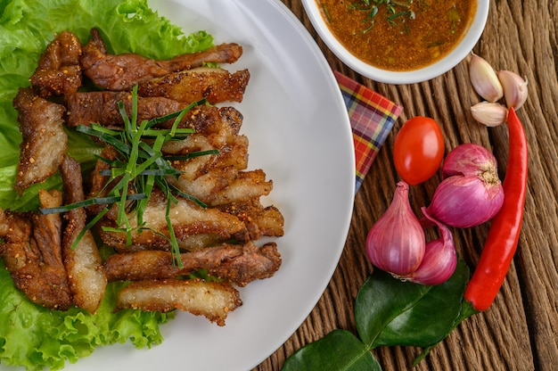 Karkówka grillowana na białym talerzu z czerwoną cebulą, pomidorem i chili na drewnianym stole.