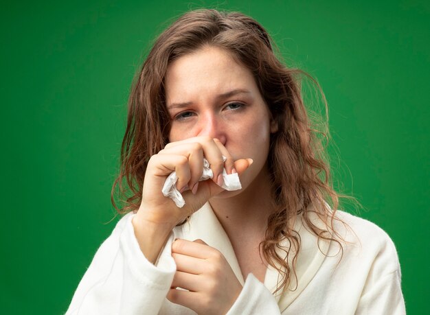 Bezpłatne zdjęcie kaszel młoda chora dziewczyna patrząc prosto przed siebie na sobie białą szatę trzymając rękę na ustach odizolowane na zielono