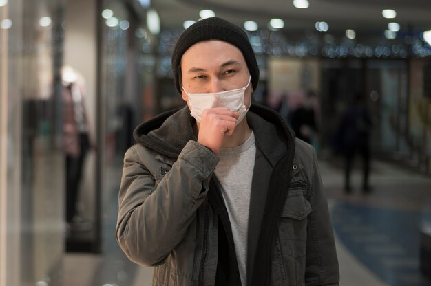 Kaszlący mężczyzna jest ubranym medyczną maskę w centrum handlowym