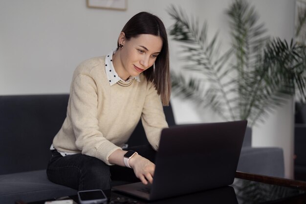 Kaukaska kobieta korzysta z laptopa siedząc na kanapie w domu w wieczornym salonie