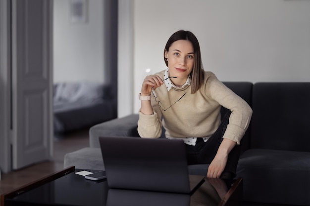 Kaukaska kobieta korzysta z laptopa siedząc na kanapie w domu w wieczornym salonie