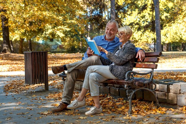 Kaukaska para starszych siedzących na ławce i czytających książkę w parku
