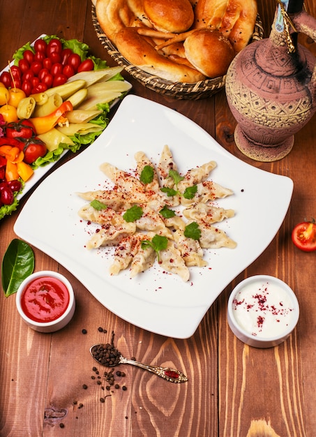Kaukaska tradycyjna żywność Dushbere, gurze podawane z jogurtem i sosem pomidorowym. w białej płytce ozdobionej turshu na drewnianym stole