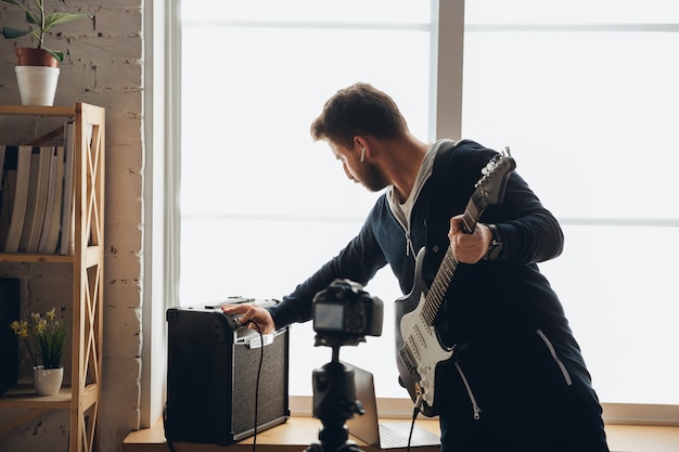 Kaukaski muzyk grający na gitarze podczas koncertu online w domu odizolowany i poddany kwarantannie, wesoły improwizujący