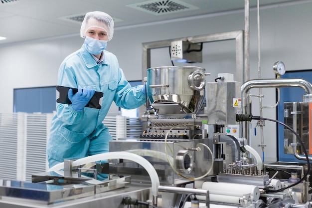 Kaukaski naukowiec w niebieskim mundurze laboratoryjnym robi notatki o dużej stalowej chromowanej maszynie, patrząc na kamerę