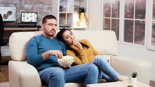 Kaukaski para relaks przed telewizorem w salonie jedzenie popcornu z frytkami.