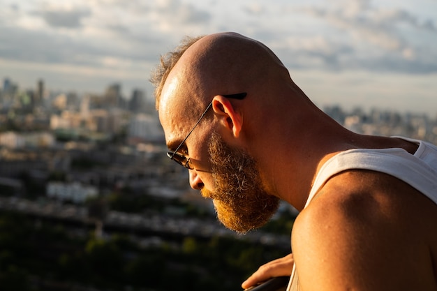 Kaukaski przystojny brodaty brutalny mężczyzna, podziwiając zachód słońca i widok na Bangkok z wysokiego piętra
