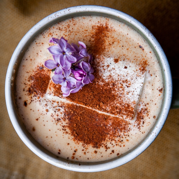 Bezpłatne zdjęcie kawa cappuccino w filiżance z płatkami kwiatów z bliska na kawałku worka