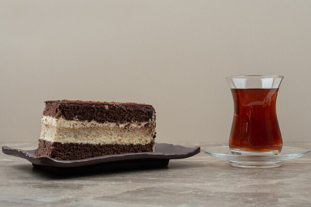 Kawałek ciasta czekoladowego i szklankę herbaty na marmurowym stole.