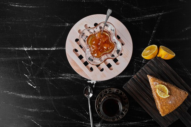 Kawałek ciasta medovic na czarnym kamieniu podawany z konfiturą i herbatą.