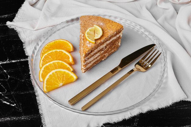 Kawałek ciasta miodowego z plastrami pomarańczy.