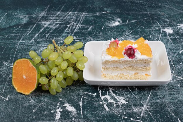 Kawałek ciasta, winogron i pomarańczy na niebieskiej przestrzeni.