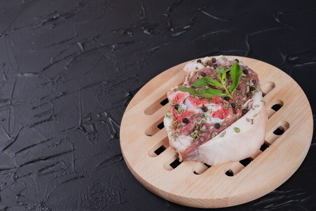 Bezpłatne zdjęcie kawałek surowego mięsa na drewnianym talerzu ozdobiony świeżą miętą na ciemnym tle.