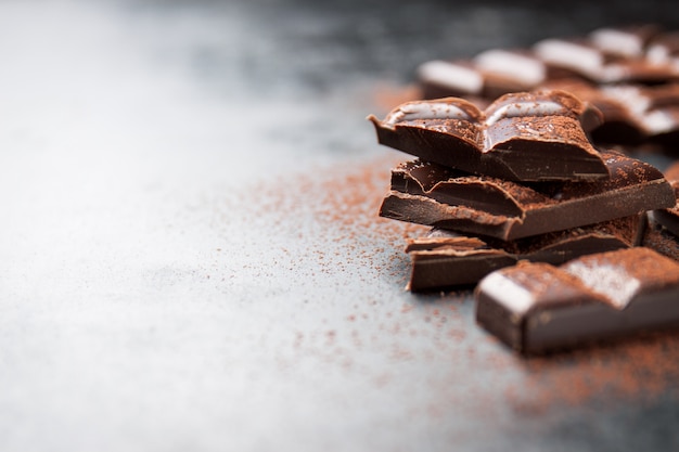 Kawałki czekolady na drewnianym stole i posypane kakao