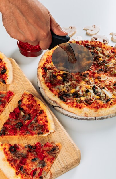 Kawałki pizzy w desce do pizzy z przyprawami, posiekane plastry grzybów i widok z góry obcinarki do pizzy na jasnoniebieskim tle