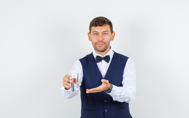 Kelner oferujący szklankę wody w koszuli, kamizelce i wyglądający wesoło.