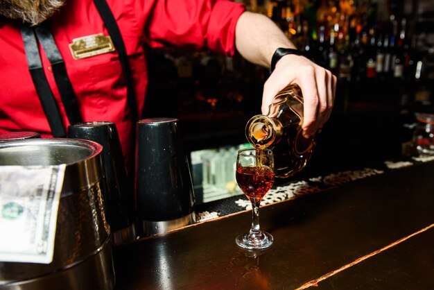 Kelner w czerwonym wylewa whisky w szklance