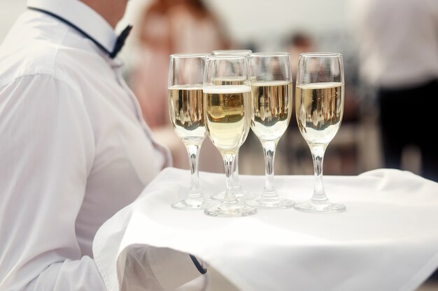 Kelner w kolorze białym nosi tacę z fletami szampana