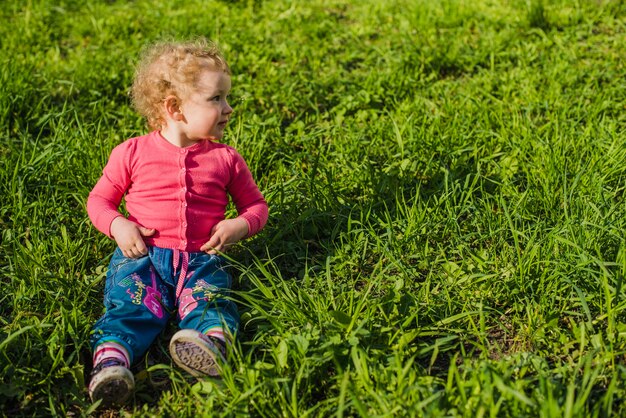 Kid siedzi na trawie i patrząc na bok