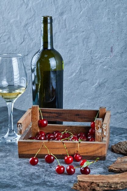 Kieliszek białego wina, butelka i drewniane pudełko wiśni na niebieskiej powierzchni