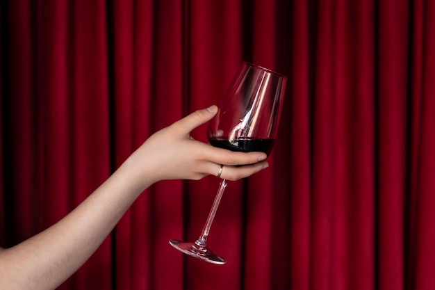 Kieliszek czerwonego wina w kobiecej dłoni na czerwonym tle tekstury