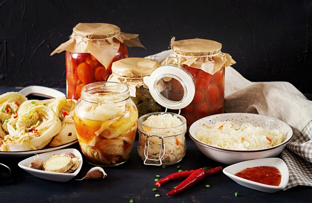 Kimchi z kapusty, marynowane pomidory, słoiki z kwaśnej szklanki na rustykalnym stole w kuchni.
