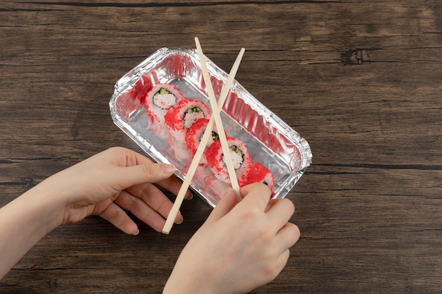 Kobiece ręce trzymające aluminiową płytkę z rolkami sushi na drewnianej powierzchni