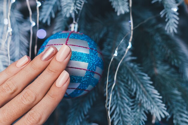 Kobiece ręce z projekt paznokci Boże Narodzenie nowy rok. Nude beżowy lakier do paznokci, błyszczący złoty brąz na jeden palec