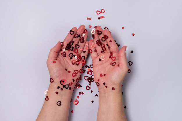 Kobiece ręce z żywym czerwonym, błyszczącym konfetti w kształcie serca na jasnoniebieskim tle