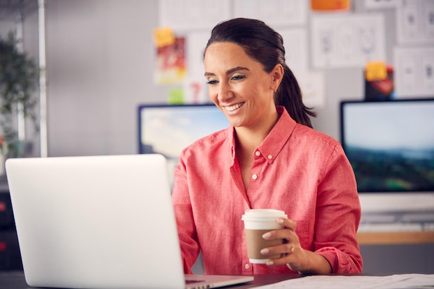 Kobiecy marketing reklamowy lub projekt kreatywny w studio pracujący na laptopie z kawą na wynos