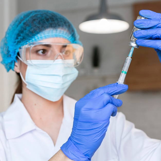 Kobieta badacz z okularami ochronnymi i maską medyczną trzymając strzykawkę i szczepionkę