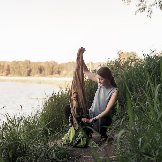 Bezpłatne zdjęcie kobieta blisko jeziora usuwa bluzę od torby