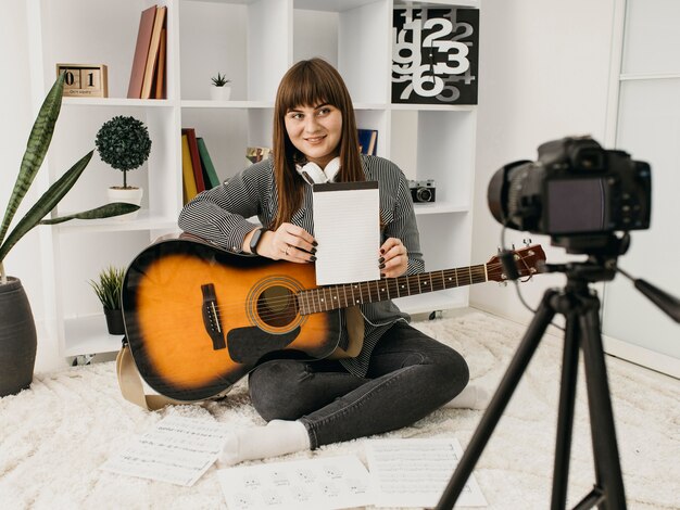 Bezpłatne zdjęcie kobieta blogerka przesyłająca strumieniowo lekcje gry na gitarze z aparatem w domu