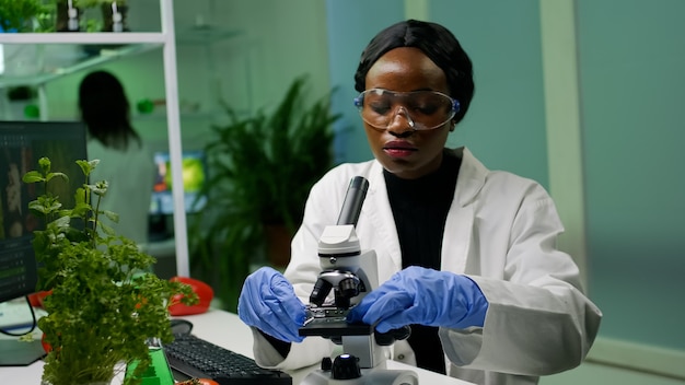 Kobieta botanik patrząca na próbkę pod mikroskopem obserwująca mutację genetyczną na roślinach