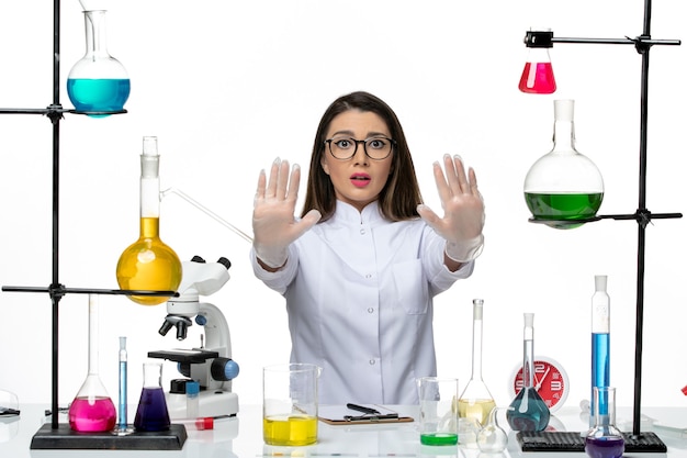 Bezpłatne zdjęcie kobieta chemik w białym garniturze medycznym siedzi z roztworami na białym biurku science pandemic virus covid lab