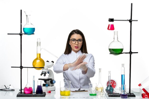 Kobieta chemik w białym kombinezonie medycznym siedząca z roztworami na białym biurku z przodu - naukowy wirus pandemiczny laboratoryjny