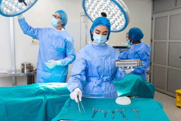 Kobieta chirurg w mundurze chirurgicznym biorąca narzędzia chirurgiczne na sali operacyjnej Młoda kobieta lekarz w szpitalnej sali operacyjnej