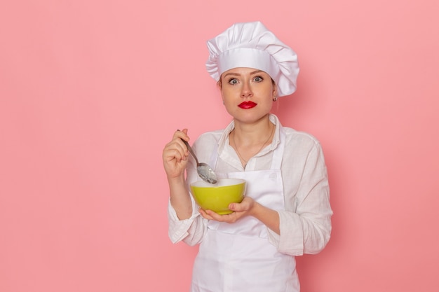 Kobieta cukierniczka w białym stroju z widokiem z przodu trzyma zielony talerz z dovga degustując go na różowym biurku posiłek posiłek zielony zupa warzywna obiad