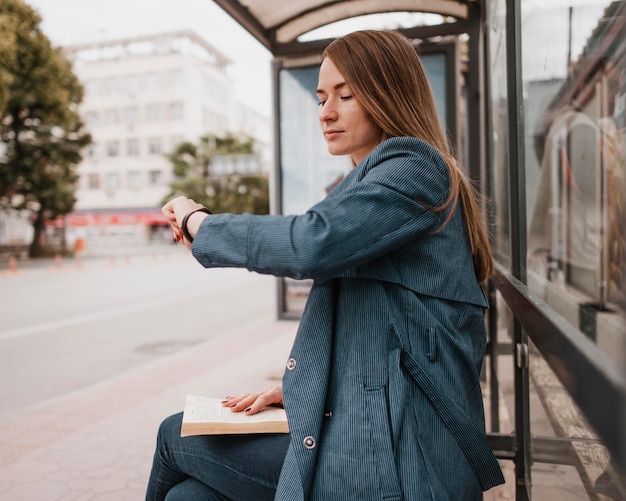 Bezpłatne zdjęcie kobieta czeka na autobus i siedzi z książką na kolanach