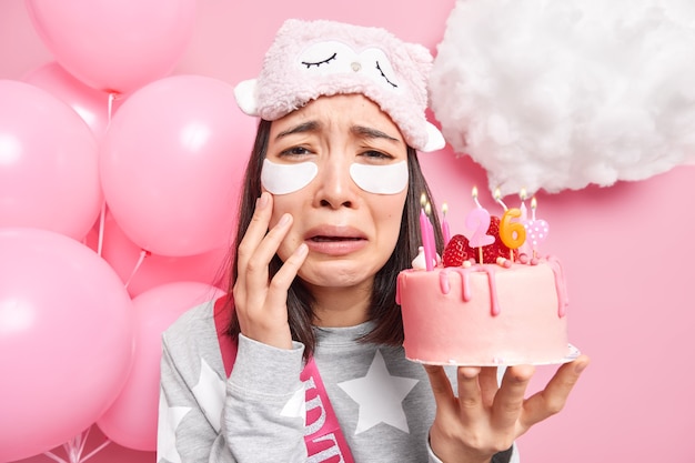 Kobieta czuje się samotna w swoje urodziny nakłada plastry pod oczy, aby pięknie wyglądać trzyma ciasto z płonącymi świeczkami