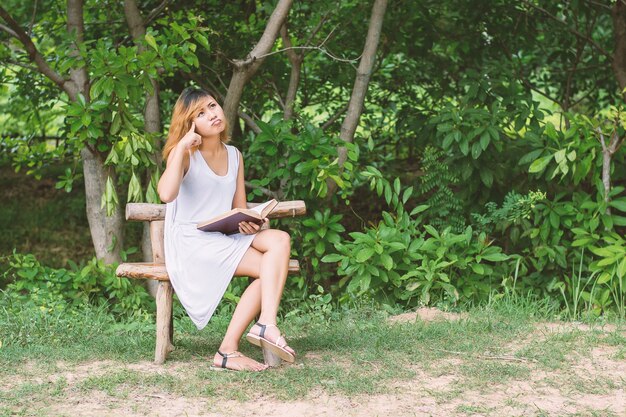 Kobieta czyta książkę siedząc na drewnianej ławce
