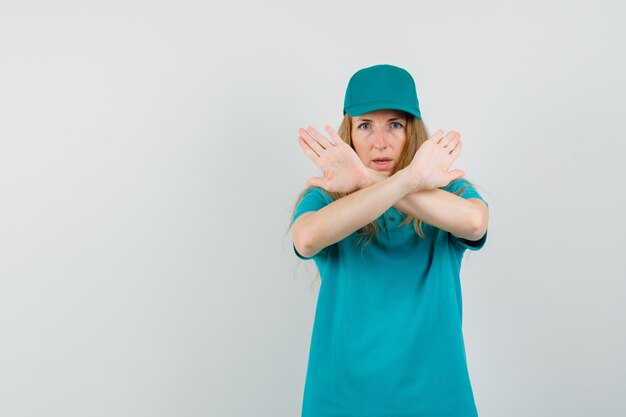 Kobieta dostawy pokazująca gest odmowy w koszulce, czapce i patrząc poważnie