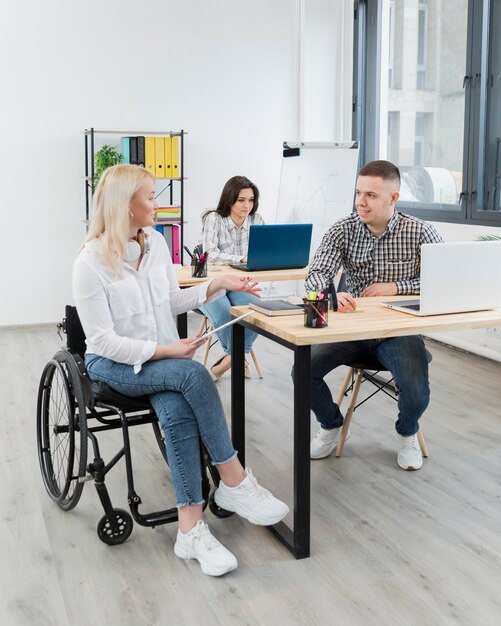 Kobieta dyskutuje z współpracownikiem przy biurkiem na wózku inwalidzkim