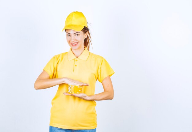 Kobieta dziewczyna w żółtym mundurze trzyma kubek z makaronem żółtym na wynos.