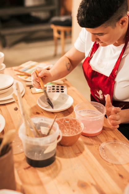 Kobieta garncarz maluje ceramiczne naczynia z pędzlem w warsztacie