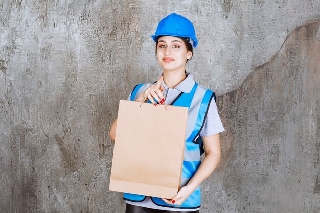 Kobieta inżynier w niebieskim kasku i narzędzi, trzymając tekturową torbę na zakupy.