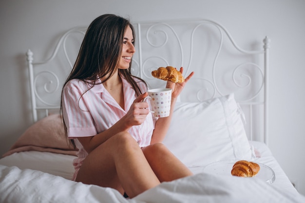 Bezpłatne zdjęcie kobieta je wyśmienicie croissant z kawą w łóżku