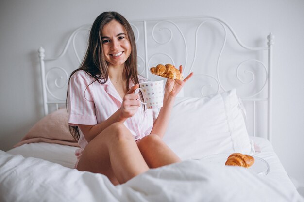Kobieta je wyśmienicie croissant z kawą w łóżku