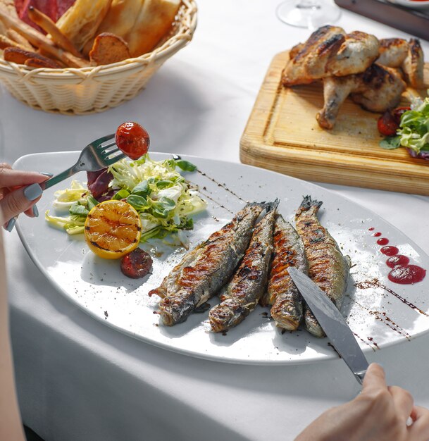 kobieta jedzenie grillowanej ryby z sałatą, grillowaną cytryną i pomidorem